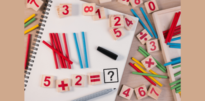 A variety of blocks and tiles showing number's are laid randomly on a desk top with pencils