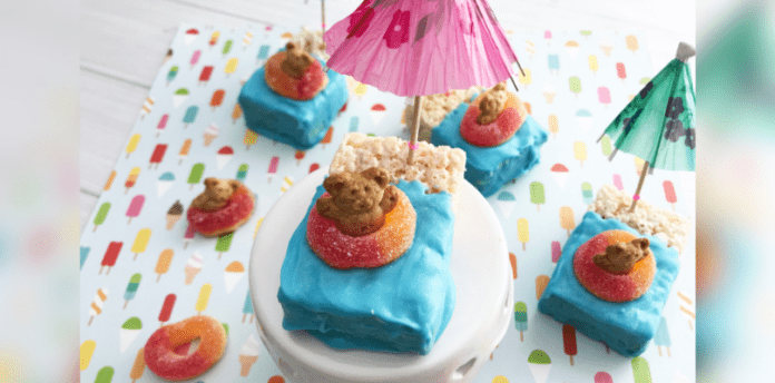 Floating Teddy Bear Rice Krispie Treats cover Floating Rice Krispie treats with teddy bears. Half of the treat is covered in blue icing and on top of the blue is a gummy ring with a grahams teddy sitting inside.